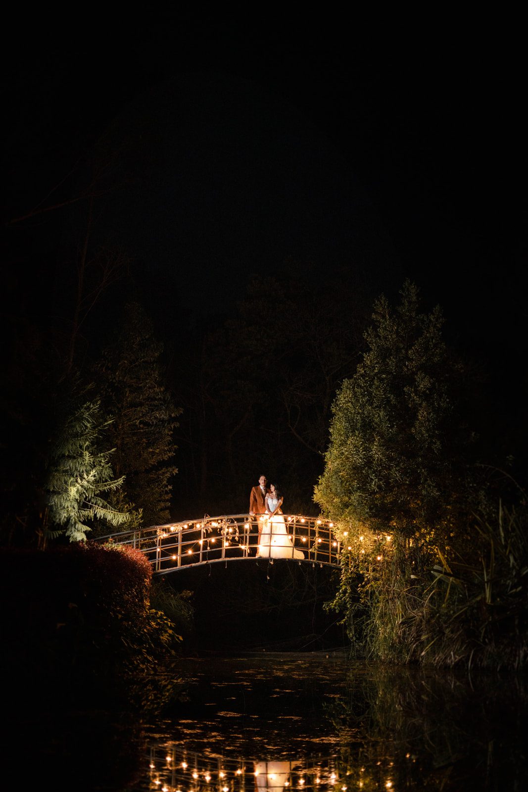 Foto nocturna de los recién casados posando románticamente en el puente iluminado de Casa Aragón.